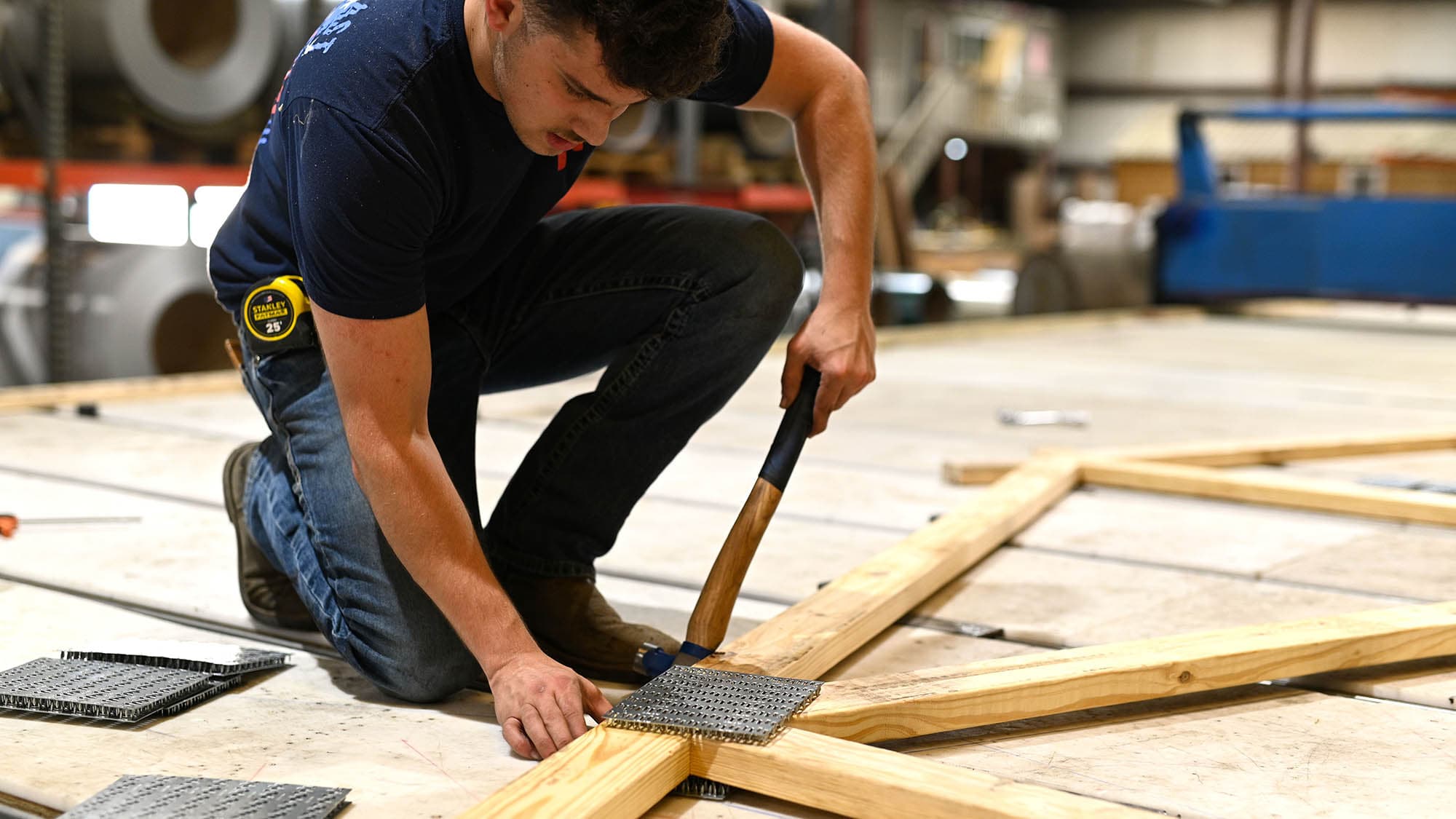 Worker driving a connector plate into a wood truss with a hammer on the assembly table at the South Boston, Virginia mill