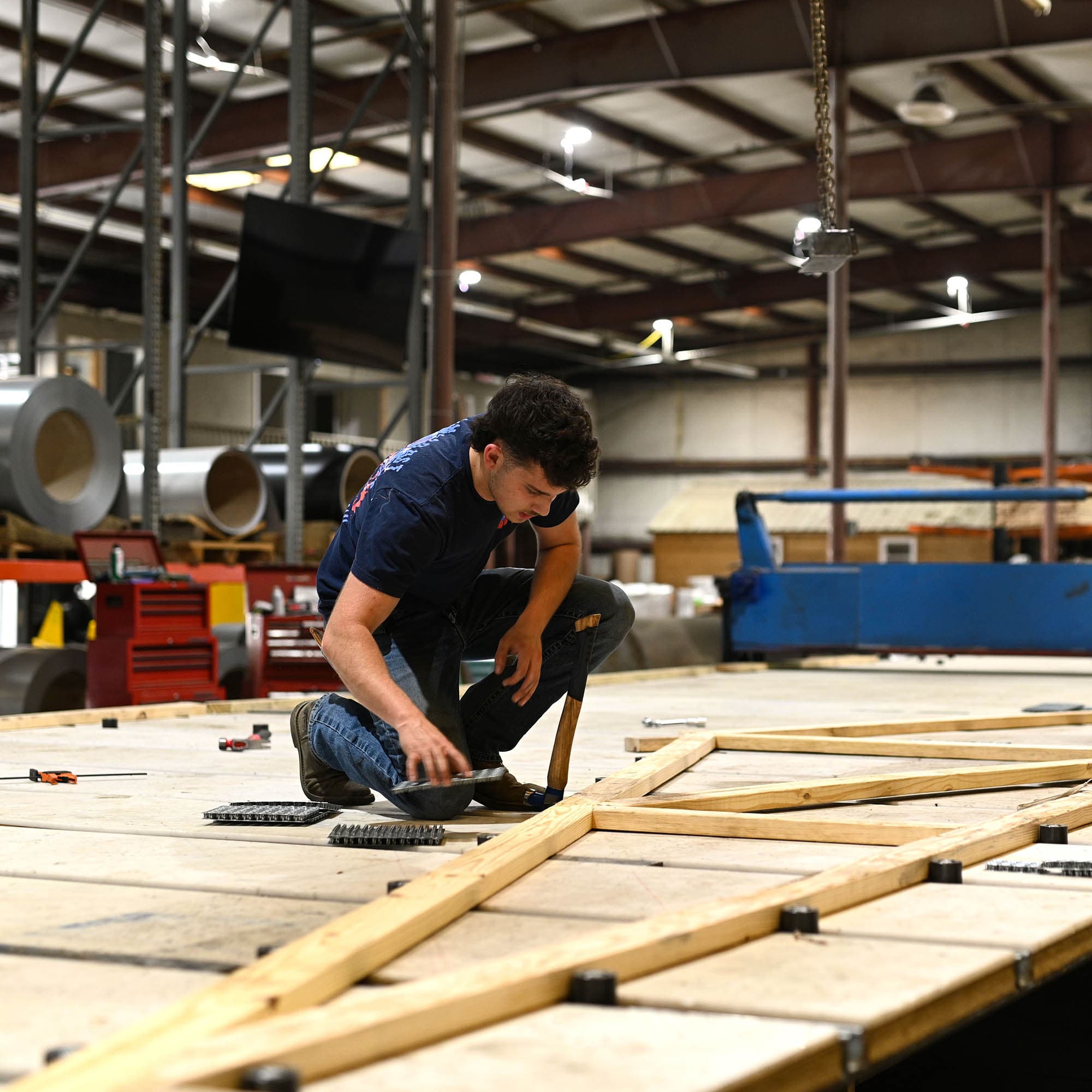 A worker driving connector plates into a wood truss on the assembly table